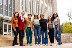 A group of smiling students stands with their arms around each other outside a building on the Bloomington campus.
